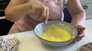 Şef bir kasede yumurta, şeker ve tereyağı çırpıyor, kek hamuru hazırlıyor.