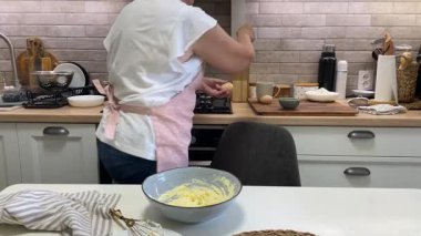 Şef bir kasede yumurta, şeker ve tereyağı çırpıyor, kek hamuru hazırlıyor.