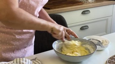 Şef bir kasede yumurta, şeker ve tereyağı çırpıyor, kek hamuru hazırlıyor.