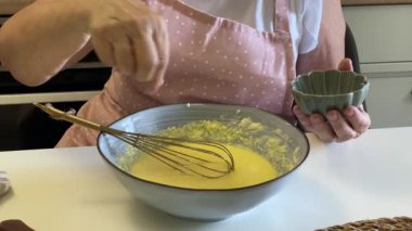 Şef bir kasede yumurta, şeker ve tereyağı çırpıyor, kek hamuru hazırlıyor.