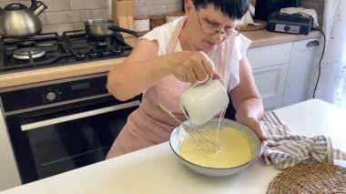 Baker bir tarifi takip eder, kasedeki diğer malzemelere süt ekler ve onları birlikte çırpar.