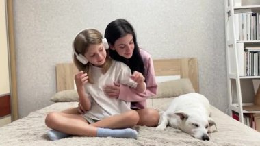 Kız kardeşler köpekleriyle yatakta oynuyorlar ve kulaklıklarını takıyorlar.