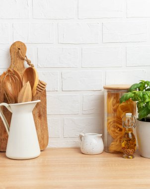 Mutfak tezgahında ahşap kaplar, makarna, fesleğen, yağ ve beyaz tuğla duvar zeminine karşı kopyalama alanı