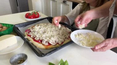 Büyükanne ve torun pizza hazırlayıp mozzarella ekliyor.