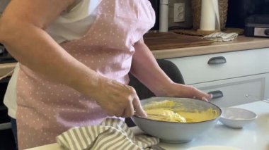 Fırıncı mutfaktaki bir kaseye hamur çırpıyor ve malzeme ekliyor.