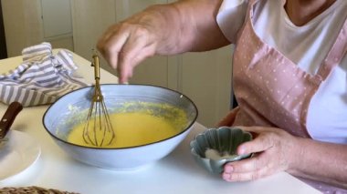 Yaşlı kadın kek karışımı hazırlıyor, tuz ekliyor ve malzemeleri bir kasede çırpıyor.