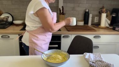 Baker bir tarifi takip eder, kasedeki diğer malzemelere süt ekler ve onları birlikte çırpar.