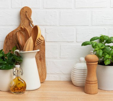 Mutfak gereçleri, fesleğen bitkisi ve ahşap tezgahta beyaz tuğladan arka planı olan baharatlar.