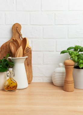 Mutfak gereçleri, fesleğen bitkisi ve ahşap tezgahta beyaz tuğladan arka planı olan baharatlar.