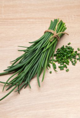 Tahta bir masada doğranmış soğan ve sicimle bağlanmış taze soğanlar.