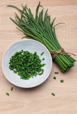 Taze soğanlar paketlenmiş ve ahşap bir yüzey üzerinde bir kasede doğranmış.