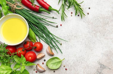 Mutfak arka planı zeytinyağı, taze bitkiler, baharatlar, kiraz domatesleri, sarımsak ve kırmızı biberler gri beton arka planda.
