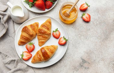 Lezzetli bir kahvaltı deneyimi için taze kruvasan, çilek, bal ve sütle servis edilir.