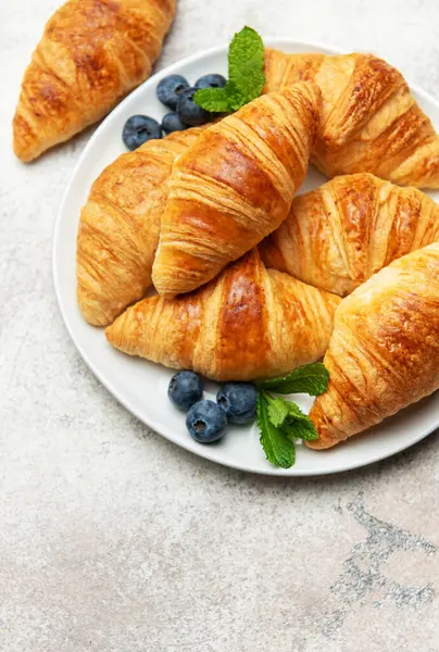 Lezzetli altın sarısı kruvasanlar taze yaban mersini ve nane yapraklarıyla beyaz bir tabakta servis edilir. Bu da cezbedici bir kahvaltı sahnesi yaratır.