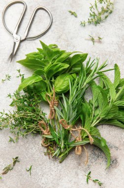 Fesleğen, biberiye, kekik ve nane içeren taze bitkiler sicimle bağlanır ve makasın yanındaki gri mermer bir yüzeye dizilir.