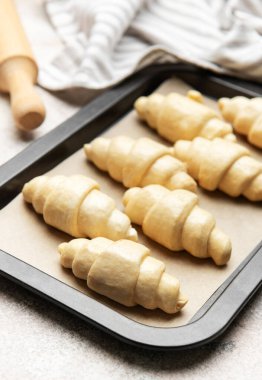 Fırın tepsisine yerleştirilmiş taze pişmemiş kruvasanlar, merdane ve mutfak havlusuyla birlikte fırına hazır.