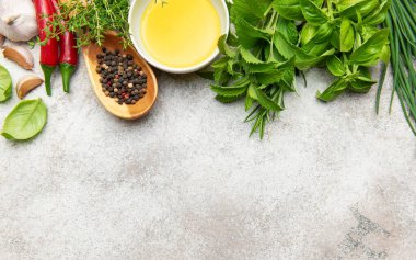Taze mutfaklar, baharatlar, sarımsak, biber ve zeytinyağı gri bir zemin üzerinde düzenlenerek yemek ve pişirme kavramları için canlı bir görüntü sunuluyor.