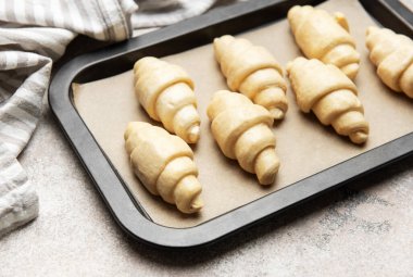 Fırınlanmamış kruvasanlar parşömen kağıdıyla kaplanmış, fırın için hazır.