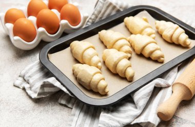 Pişirilmeye hazır yumurta ve oklavalı ekmek tepsisi üzerinde çiğ kruvasan.