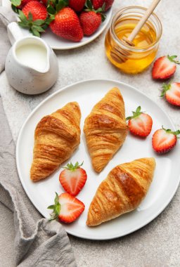 Lezzetli bir kahvaltı deneyimi için taze kruvasan, çilek, bal ve sütle servis edilir.