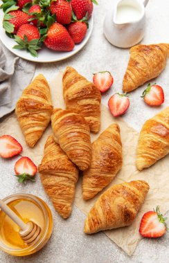 Lezzetli altın rengi kruvasanlar taze çilek, bal ve sütle servis edilir. Bu da cezbedici bir kahvaltı sahnesi yaratır.