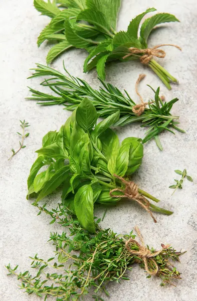 Taze nane, kekik, biberiye ve iplikle bağlanmış fesleğen demetleri desenli bir yüzeyde duruyor.