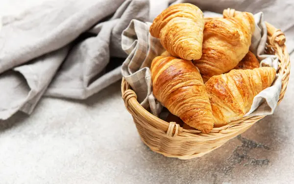 Taze pişmiş kruvasanlar kırsal bir masada hasır sepetin içinde dinleniyor.