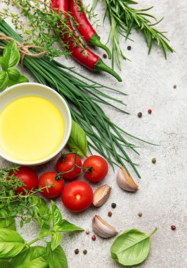 Mutfak arka planı zeytinyağı, taze bitkiler, baharatlar, kiraz domatesleri, sarımsak ve kırmızı biberler gri beton arka planda.