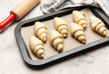 Fırın tepsisine yerleştirilmiş taze pişmemiş kruvasanlar, merdane ve mutfak havlusuyla birlikte fırına hazır.