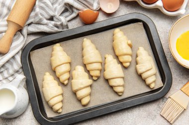 Pişirme çarşafında çiğ kruvasan, fırın için hazır, malzemeler ve aletlerle.