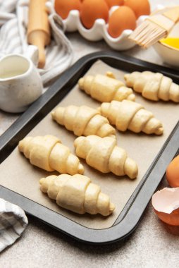 Pişirme çarşafında çiğ kruvasan, fırın için hazır, malzemeler ve aletlerle.