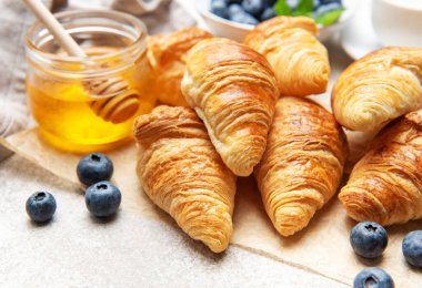 Lezzetli altın sarısı kruvasanlar yabanmersini, bal ve sütle servis edilir ve nefis bir kahvaltı hazırlar.
