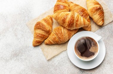 Kahverengi kruvasanlar parşömen kağıdının üzerinde buharı tüten bir fincan kahvenin yanında, nefis bir kahvaltı deneyimini somutlaştırıyorlar.