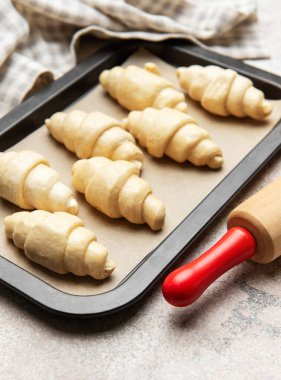 Fırın tepsisine yerleştirilmiş taze pişmemiş kruvasanlar, merdane ve mutfak havlusuyla birlikte fırına hazır.