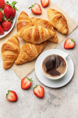 Taze pişmiş kruvasan, bir fincan dumanı tüten kahve ve nefis bir kahvaltı sahnesi yaratan sulu çilekler.