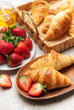 Taze pişmiş kruvasan çilek ve bal ile servis edilir, nefis bir kahvaltı hazırlar.