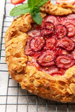 Badem gevreği ve nane yapraklarıyla süslenmiş taze pişmiş çilek galeti, tel askıda soğutuluyor.