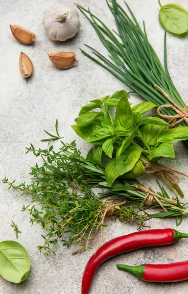 Gri arka planda taze toplanmış otlar ve baharatlar canlı bir mutfak malzemesi gösterisi yaratıyor.