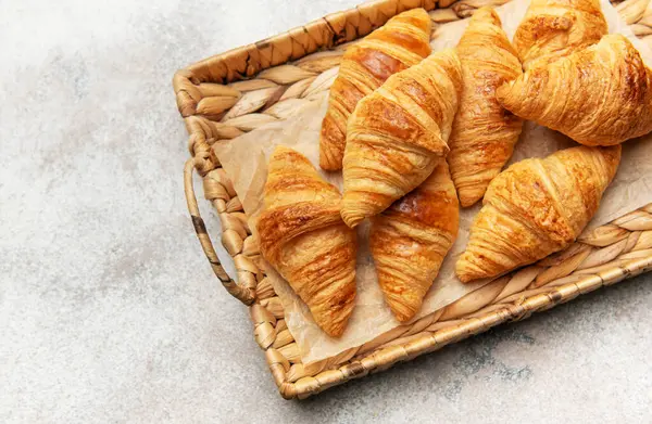 Hasır bir tepside dizilmiş altın rengi kruvasanlar cezbedici bir kahvaltı ya da kahvaltı hazırlıyor.
