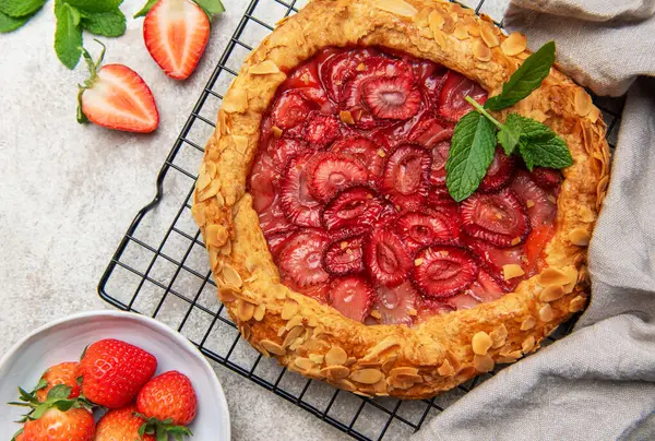 Badem gevreği ve nane yapraklarıyla süslenmiş taze pişmiş çilek galeti, tel askıda soğutuluyor.