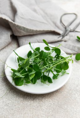 Taze bezelyeler beyaz bir tabakta makas ve desenli bir arka planda keten peçeteyle filizlenir.