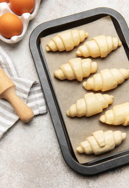 Pişirilmeye hazır yumurta ve oklavalı ekmek tepsisi üzerinde çiğ kruvasan.