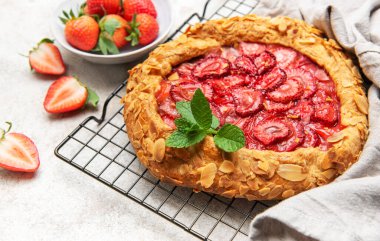 Nane yapraklarıyla süslenmiş taze pişmiş çilek galeti ve soğutma rafında duran badem gevrekleri.