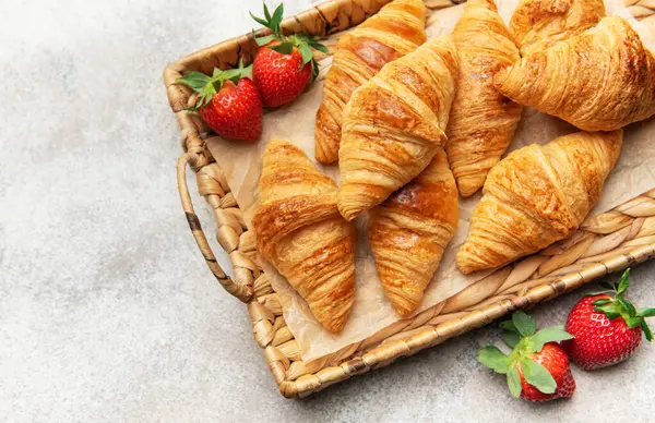 Altın sarısı kruvasan ve hasır tepside hazırlanmış olgun kırmızı çilekler çok cazip bir kahvaltı sunuyor.