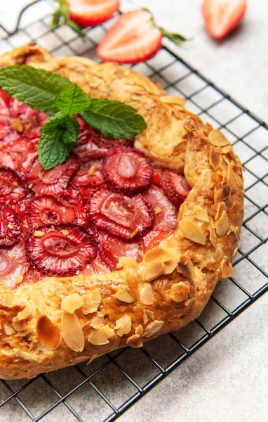 Badem gevreği ve nane yapraklarıyla süslenmiş taze pişmiş çilek galeti, tel askıda soğutuluyor.