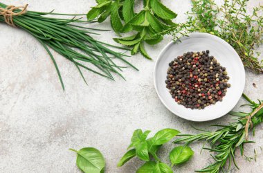 Frenk soğanı, fesleğen, nane, kekik ve biberiye gibi taze bitkiler dokulu bir mutfak masasındaki karışık biber kasesinin etrafına dizilmiştir.