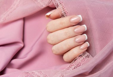 Pembe arka planda dantelli Fransız manikürünü gösteren bir kadın.