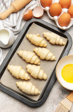 Pişirme çarşafında çiğ kruvasan, fırın için hazır, malzemeler ve aletlerle.