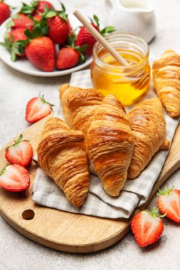 Taze pişmiş kruvasanlar lezzetli bir kahvaltı için ahşap bir tahtada çilek ve bal ile servis edilir.