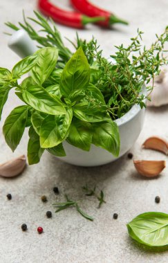 Havan ve kabuk taze fesleğen, kekik ve biberiye ile taşar, yanında da sarımsaklı karanfil, biberli ve biberli biberli mutfak masasında.